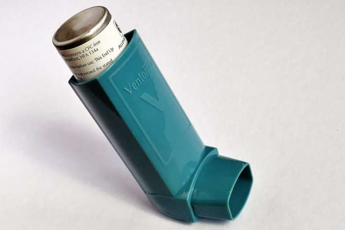 A standard green-colored asthma inhaler with grey background.