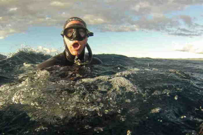 Freediver on water surface inhaling while wearing black mask and wetsuit.