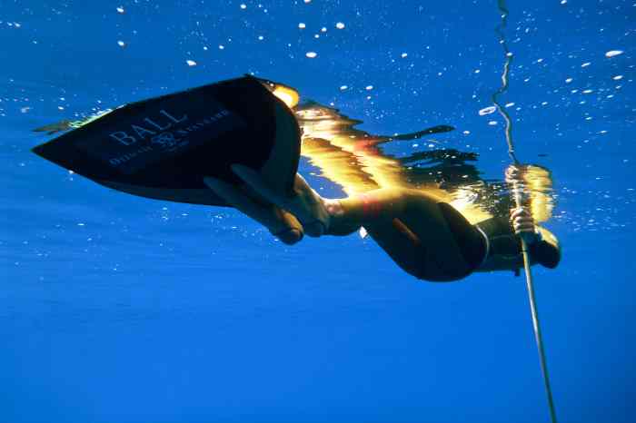 Freediver laying on back underwater, near surface of water wearing monofin.