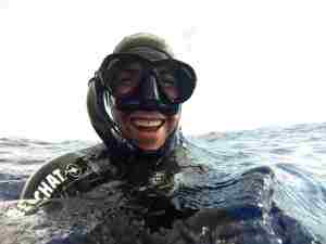 Freediver in the ocean smiling while wearing black snorkel and black mask
